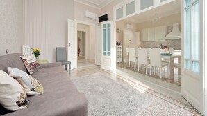 A spacious living room with a grey sofa, a patterned rug, and a dining area with white chairs and a table.