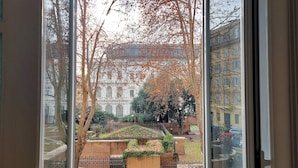 A view through a window of a park with a fountain, trees, and buildings in the background.