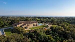 A stone villa with a swimming pool, surrounded by lush greenery and a view of the city in the distance.