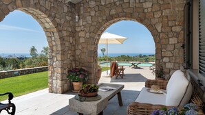 A stone-arched outdoor patio with a pool, lounge chairs, and a table with a book and flowers.