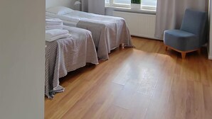 Una habitación con dos camas, una silla y un ventanal con cortinas.