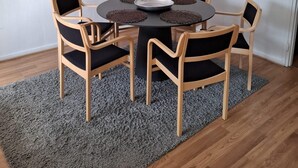 Un comedor con una mesa redonda, seis sillas de madera con cojines negros, un mantel negro y una lámpara de pie.