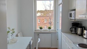 Una cocina estrecha con gabinetes blancos, una mesa blanca y una ventana con vistas a edificios.