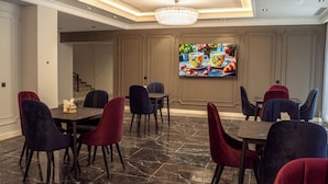 A dining area with a chandelier, a television on the wall, and a staircase in the background. - Meridian Plaza by Reikartz (Samarkand)