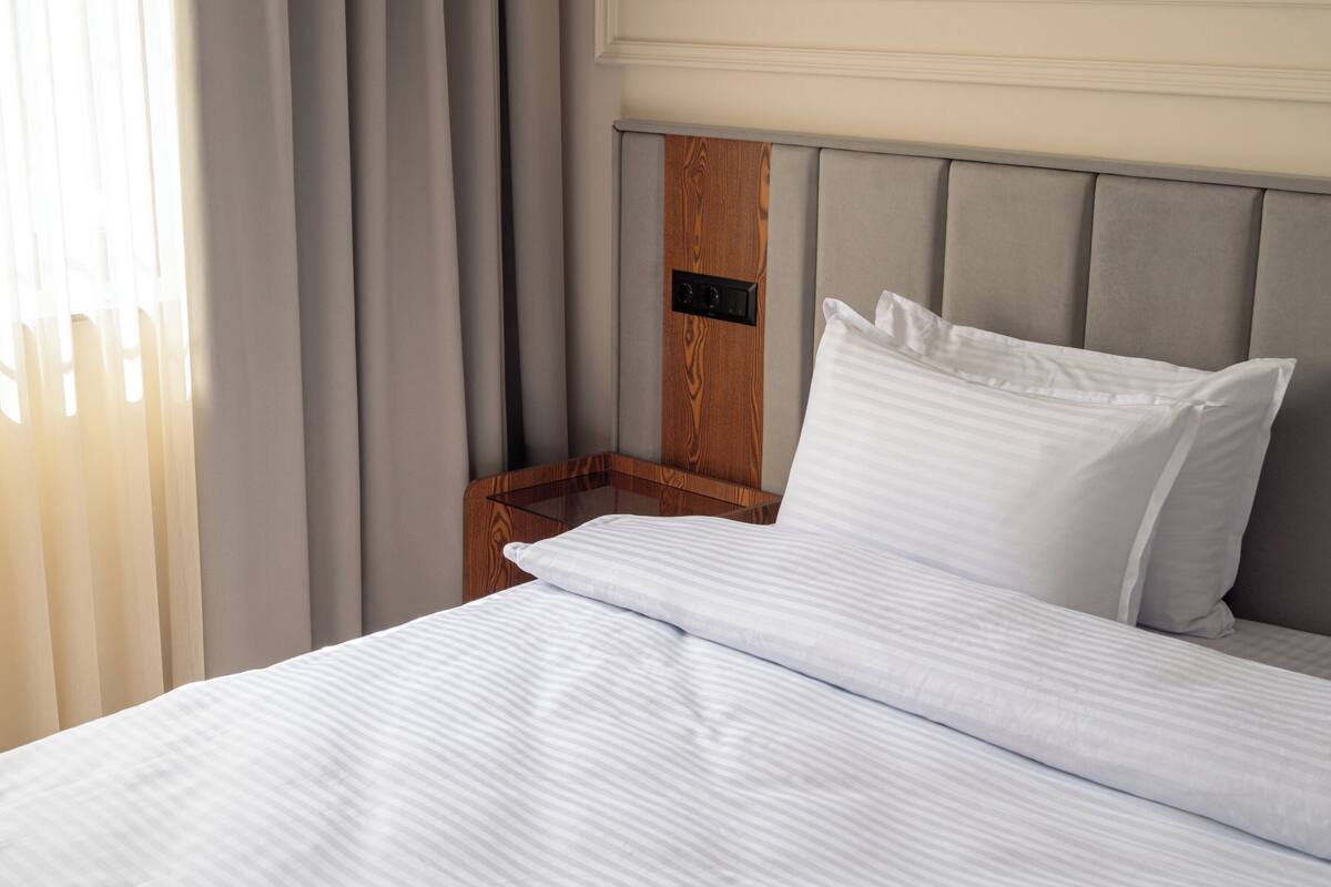 A neatly made bed with white linens and a wooden headboard.