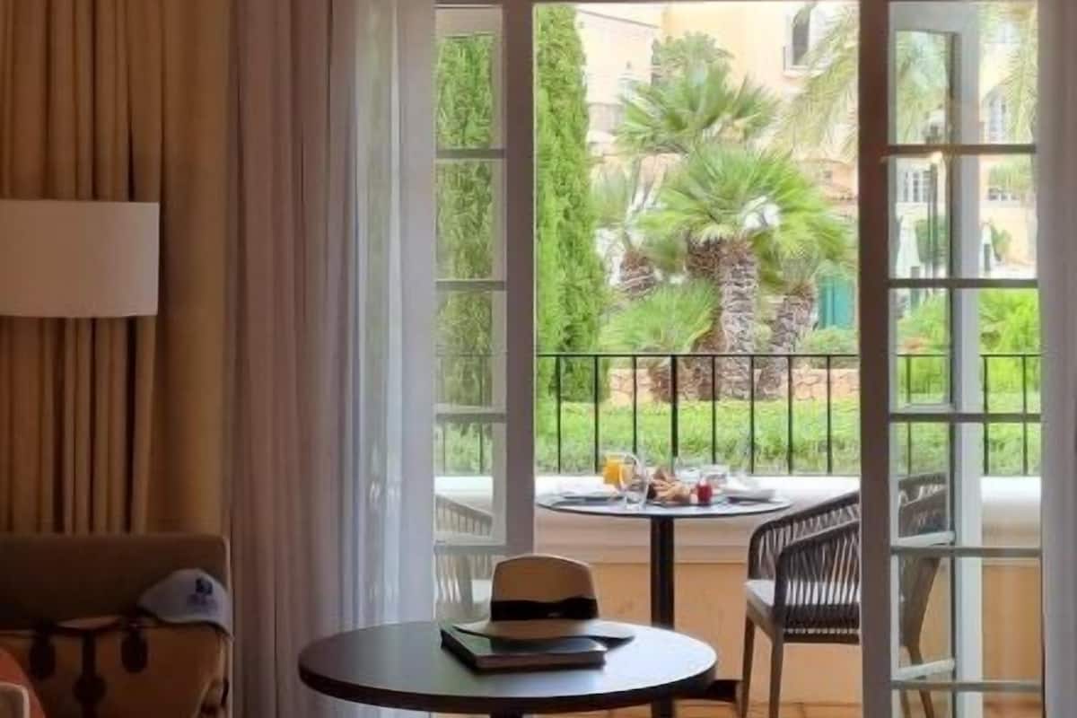 Habitación de hotel con sofá, una mesa y un libro, y vistas a un patio con una palmera.
