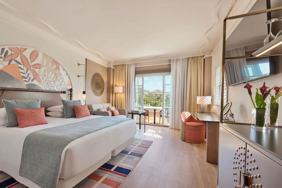 Ein Hotelzimmer mit einem Bett, einem Schreibtisch, einem Stuhl, einem Fernseher und einem Balkon mit Blick.