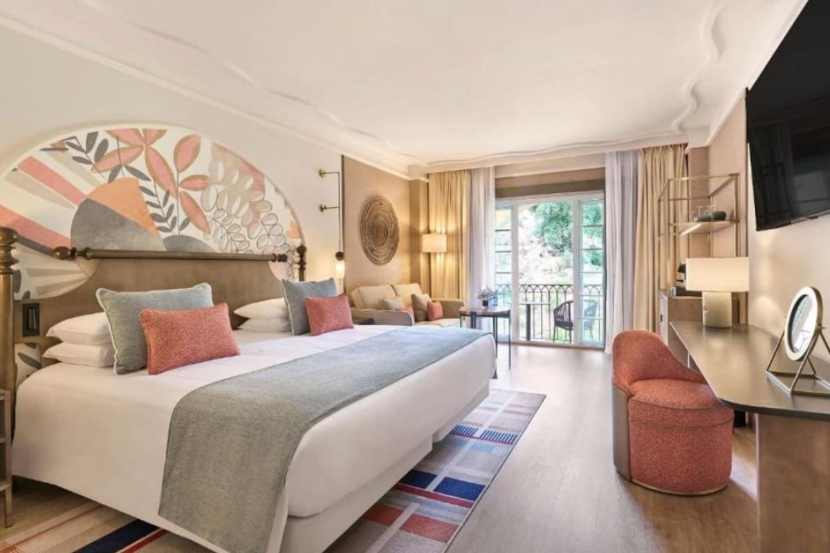 Ein Hotelzimmer mit Bett, Schreibtisch, Stuhl, Fernseher und Balkon.