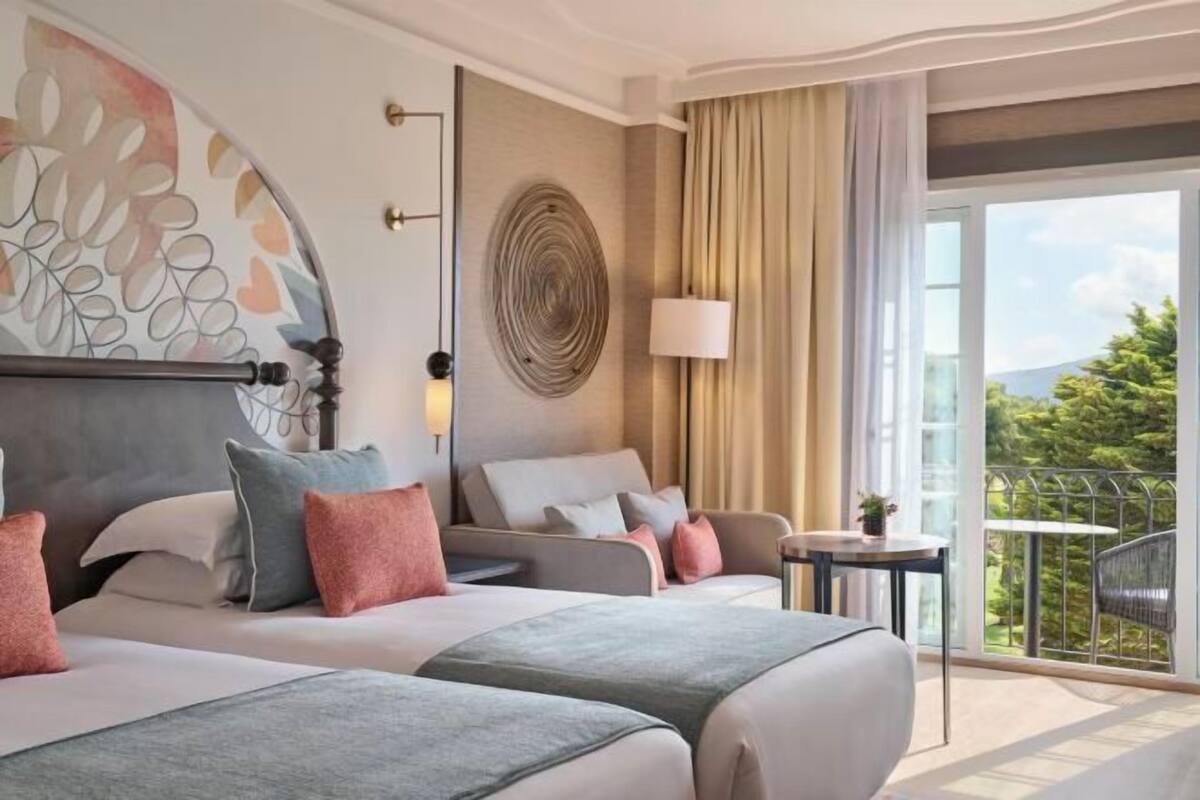 Habitación de hotel con dos camas, un balcón con vistas, un adorno redondo en la pared y una lámpara.