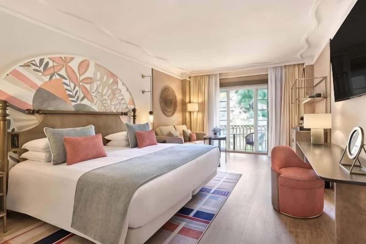 Una habitación de hotel con una cama grande, un escritorio, una silla, un televisor y un balcón con vistas.