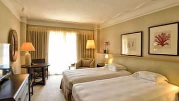 A hotel room with two beds, a desk, a chair, and a lamp.