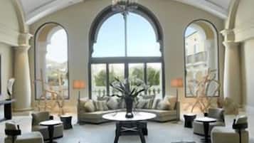 A spacious lounge area with a central round table, multiple seating options, and large arched windows providing a view.