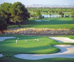 Ein Golfplatz mit Sandbunkern, einer Steinmauer und einem großen Baum.