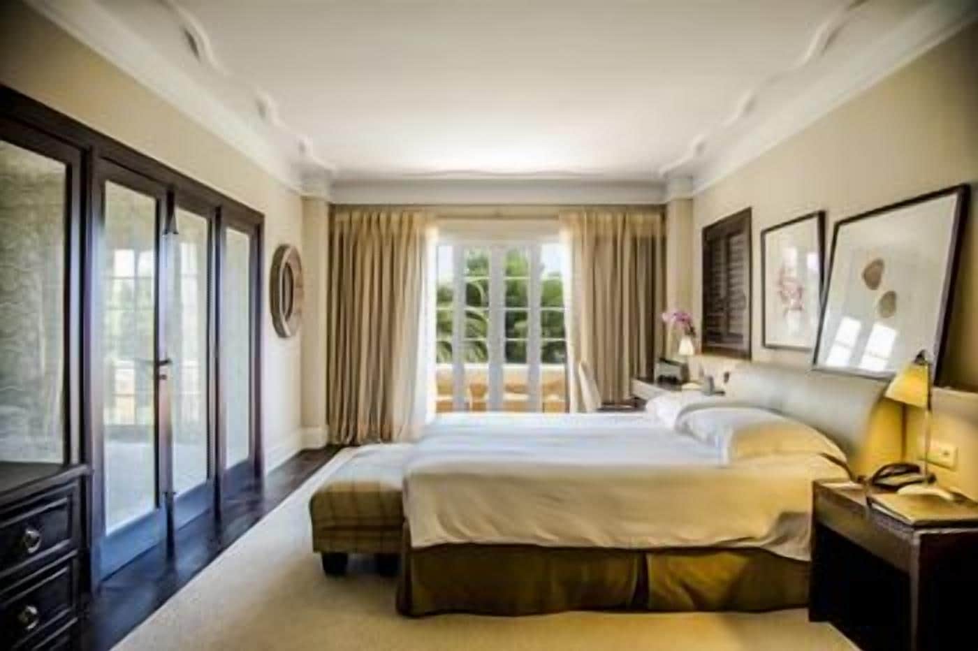A hotel room with a large bed, a nightstand, a lamp, and a view of the outdoors.