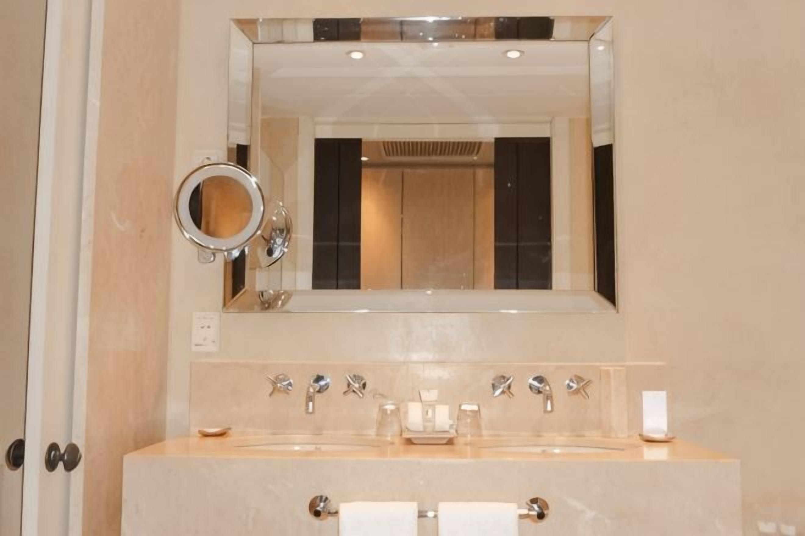 A bathroom with a large mirror, a sink with multiple faucets, and a towel rack.