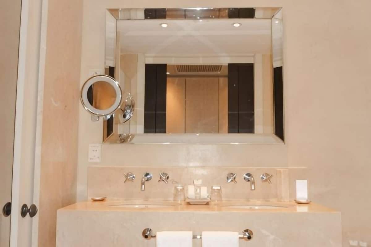 Un baño con un espejo grande, un lavamanos con múltiples grifos y un perchero para toallas.