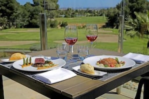 Ein Tisch ist mit Speisen und Weingläsern gedeckt, mit Blick auf einen Golfplatz.