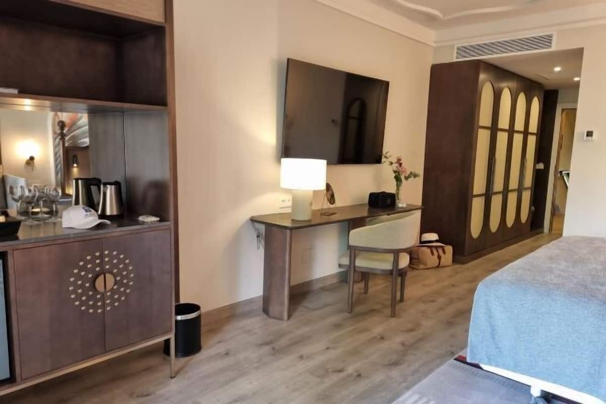 Habitación de hotel con cama, escritorio con lámpara, una silla, cómoda y espejo.