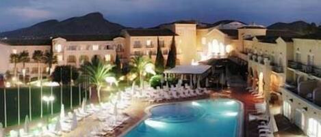 A hotel with a swimming pool, lounge chairs, and a mountain backdrop.
