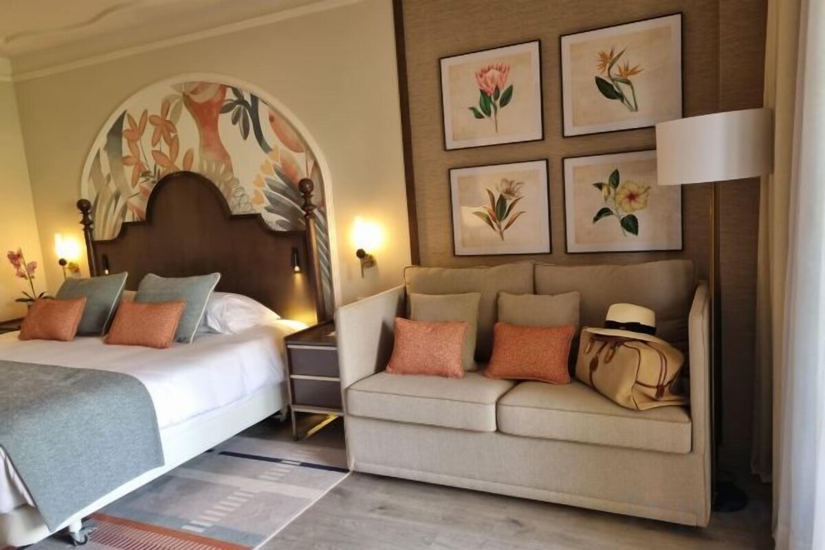 Habitación de hotel con cama, sofá, mesita de noche y lámparas de pared.