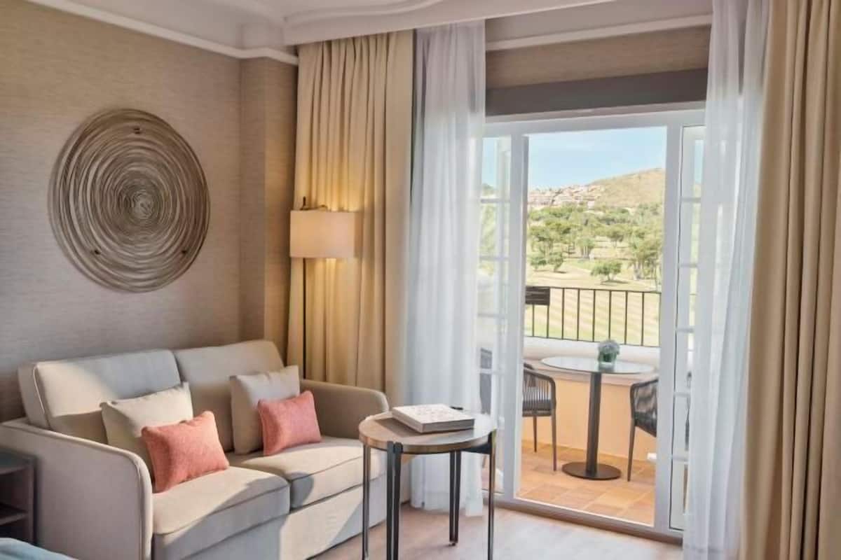 Habitación de hotel con sofá, una mesita, una lámpara y vistas al exterior.
