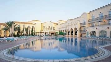 A pool surrounded by buildings with balconies, palm trees, and a clear sky.