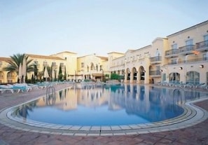 A pool surrounded by buildings with balconies, palm trees, and a clear sky. - Grand Hyatt La Manga Club Golf & Spa (Murcia)