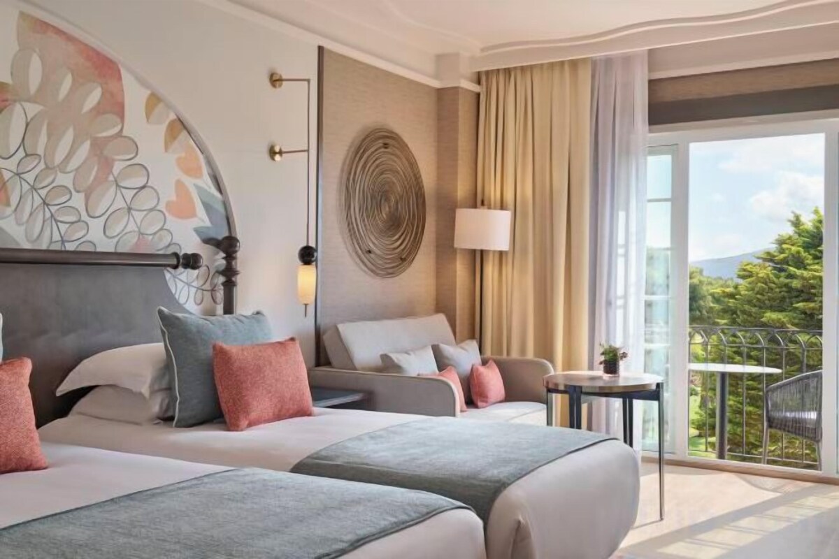Habitación de hotel con dos camas, un balcón y vistas al exterior.