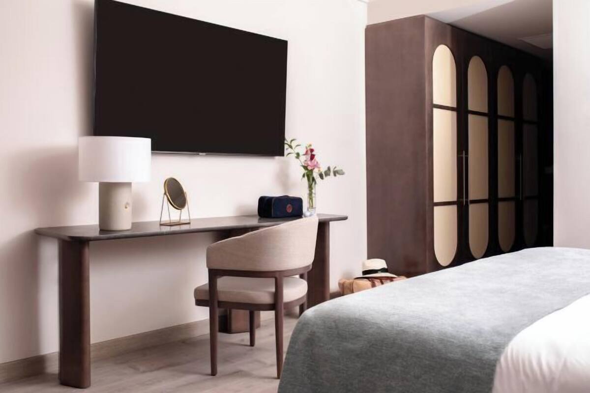 Habitación de hotel con cama, escritorio con silla, televisor montado en la pared y armario de diseño único.