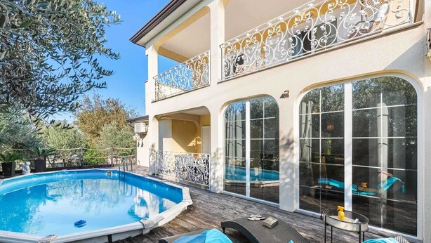 An outdoor swimming pool with a wooden deck, lounge chairs, and a large house with ornate balconies and large windows. - VILLA SEABIRD Holiday House with Private Pool (Nova Vas)