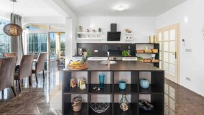 A modern kitchen with a central island, built-in shelves, and a dining area with wicker chairs. - VILLA SEABIRD Holiday House with Private Pool (Nova Vas)