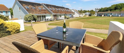 A deck with wicker furniture and a table, overlooking a residential area with houses and a grassy field.