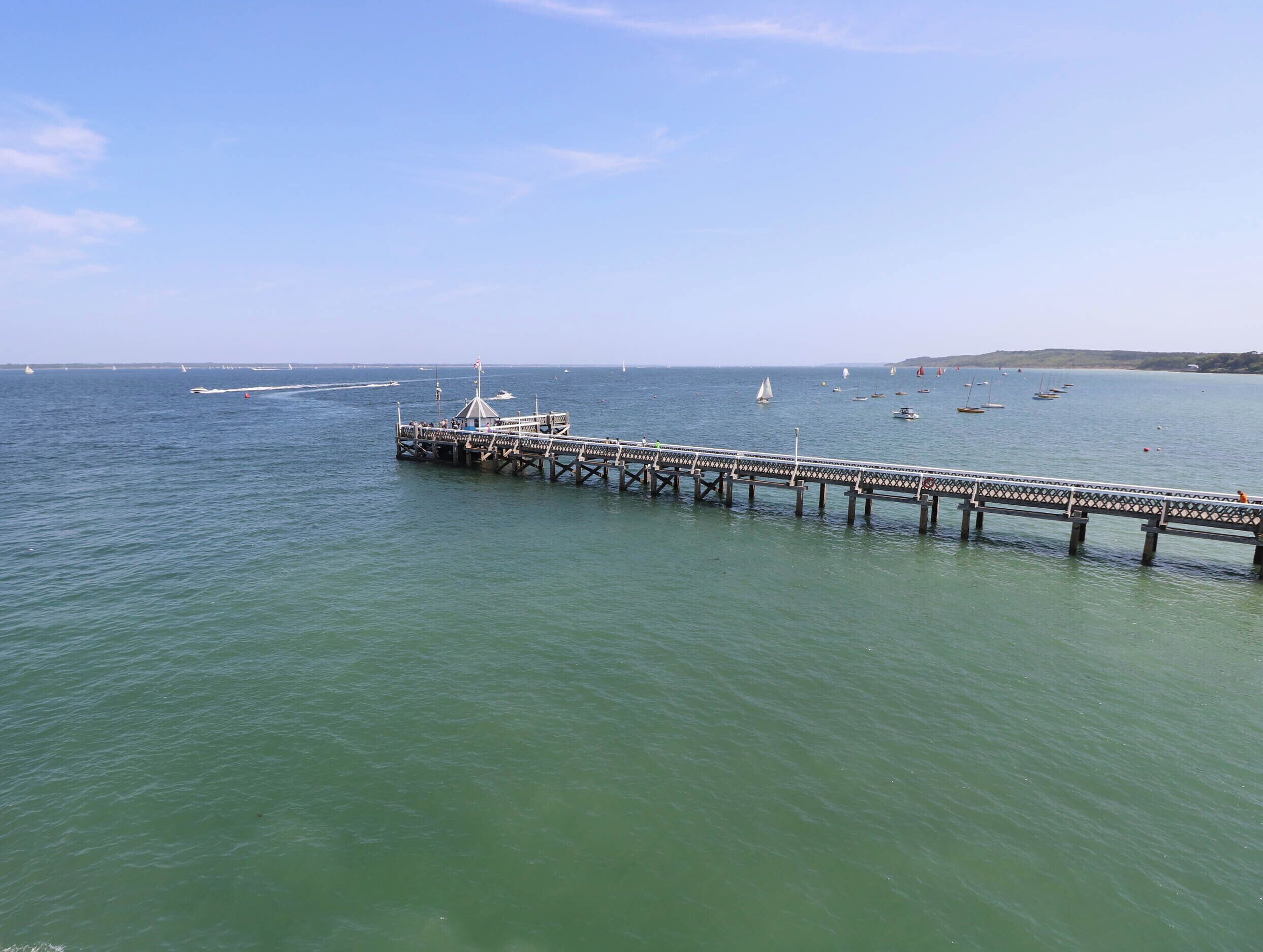 Eine Pier, die sich in ruhiges Wasser erstreckt, mit Booten und wolkenlosem Himmel.