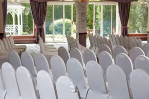 A room with rows of white chairs, large windows, and a white gazebo outside.