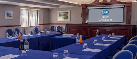 A conference room with tables, chairs, and a projector screen displaying 'BW Best Western.'