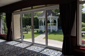 Una habitación con un amplio ventanal corredizo que da a un patio con un pabellón y un césped.