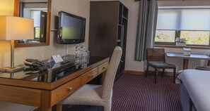 Habitación de hotel con escritorio, silla, cama, televisor y ventana con vistas.