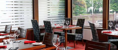 A restaurant with tables set for dining, chairs, and wine glasses.