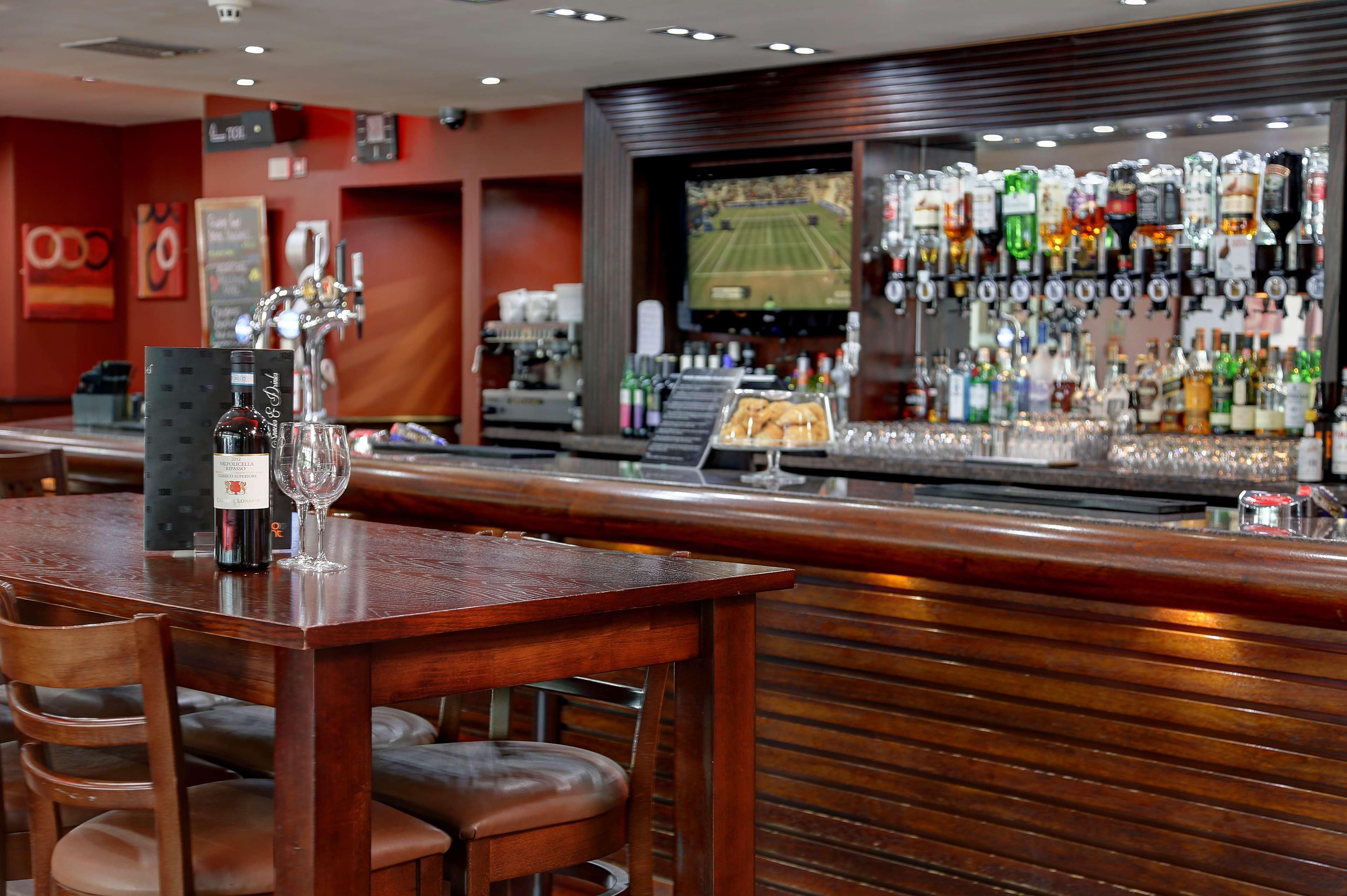 A bar area with a wooden counter, stools, and a variety of bottles and glasses.