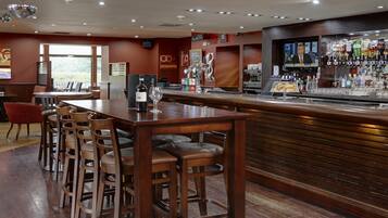 A bar area with stools, a counter, and a television screen displaying a news channel.