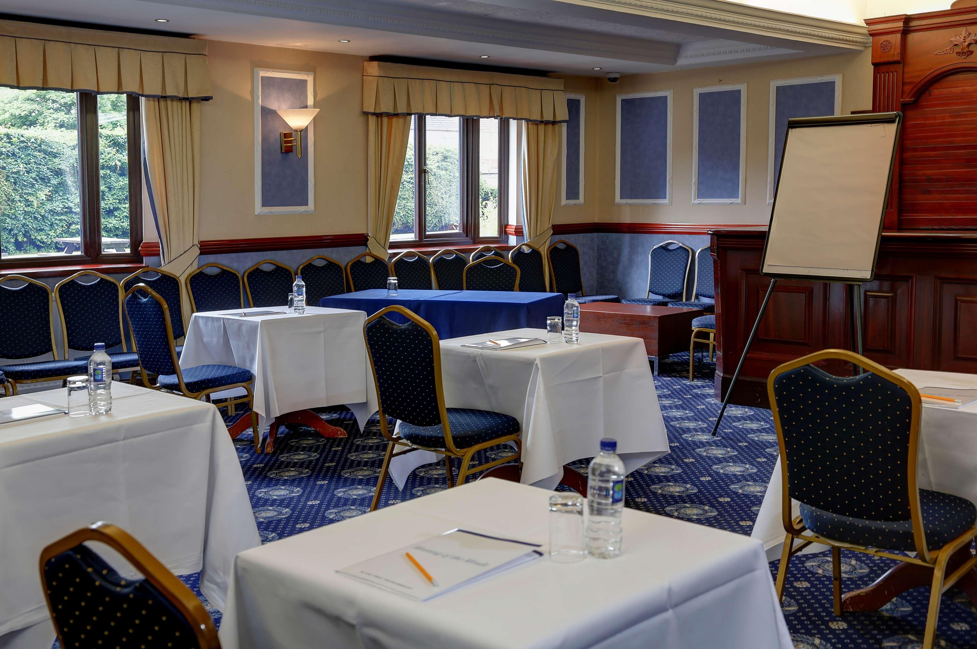 A conference room with tables, chairs, a whiteboard, and a view of trees through the windows.