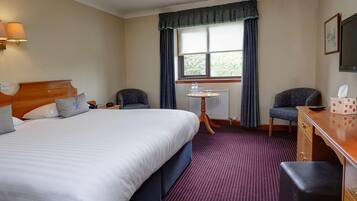 A hotel room with a large bed, two chairs, a desk, and a window with curtains.
