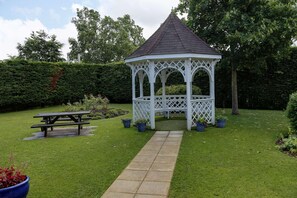 A gazebo with a tiled roof and lattice design, a picnic table, and a stone pathway.