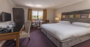 Habitación de hotel con cama, escritorio, silla, televisor y ventana con cortinas.
