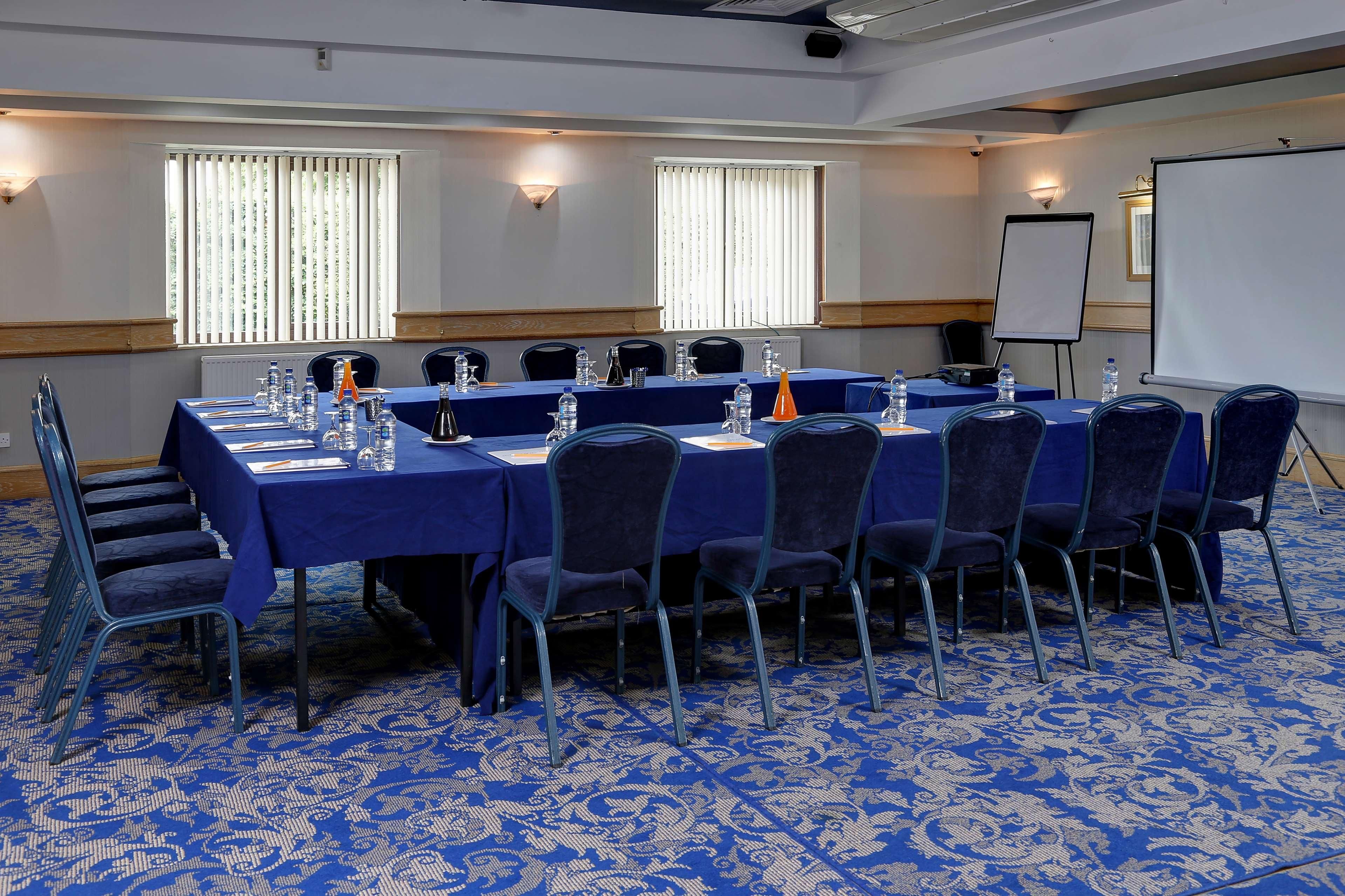 A conference room with a long table, chairs, water bottles, and a projector screen.