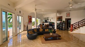 A spacious living area with a black sectional sofa, a coffee table, and a staircase with a wooden railing. - Central Villa, big spaces, 180° Seaview with infinite Pool con hot Jacuzzi (Las Terrenas)