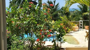 A view of a pool area with palm trees and flowering plants. - Central Villa, big spaces, 180° Seaview with infinite Pool con hot Jacuzzi (Las Terrenas)