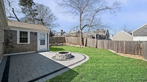 A backyard with a paved patio, a stone fire pit, and a wooden fence.