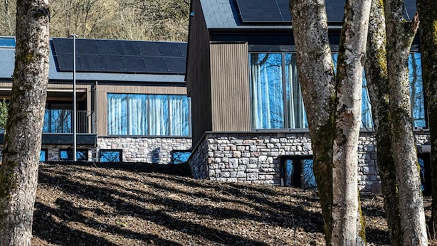 A modern building with solar panels on the roof, stone walls, and large windows.