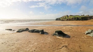 A beach with rocky outcrops and a distant view of a fortified structure on a cliff. - Lacey's Harbour (Battlestown)